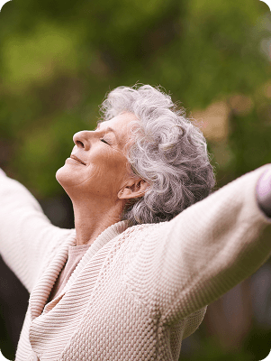 Older woman standing with arms raised outdoors