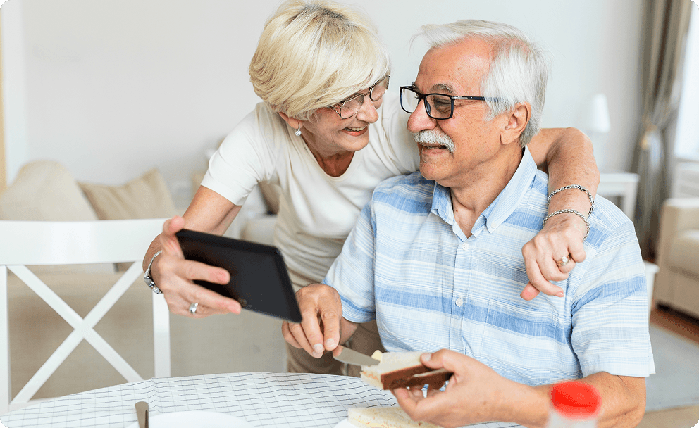 Older couple smiling while looking at a tablet together on a couch